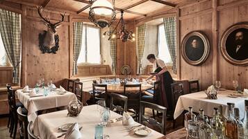 A wooden interior with tables set for dining, a chandelier, and framed portraits on the walls.