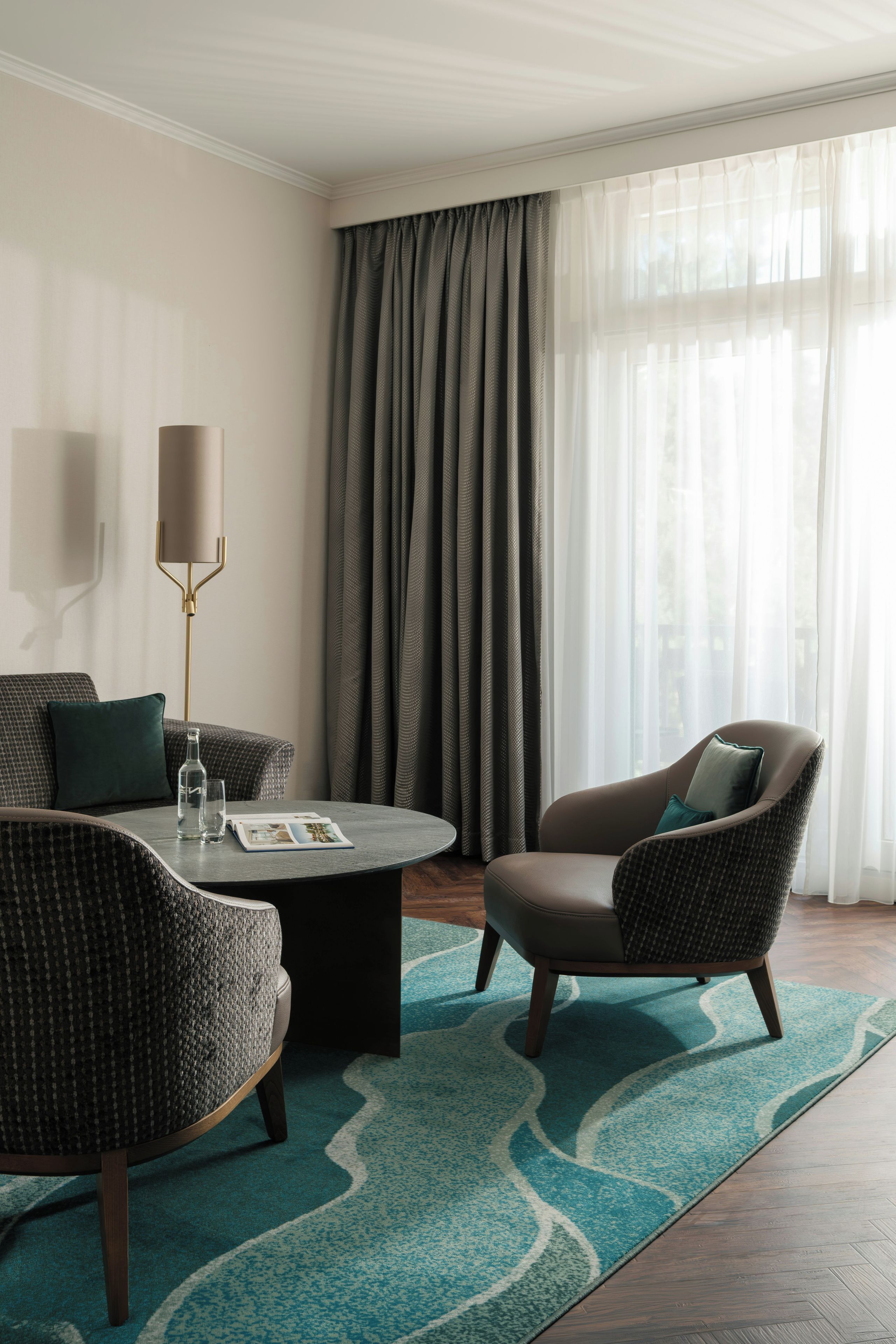 A modern hotel room with a sofa, armchair, and a coffee table with magazines.