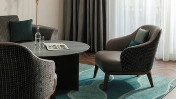 A modern hotel room with a sofa, armchair, and a coffee table with magazines.