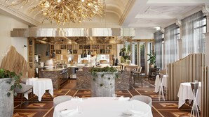 A spacious dining area with round tables, a central island with bar stools, and a modern chandelier.