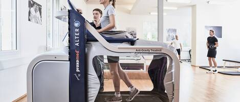 A treadmill with a digital display, a person using it, and another person observing.