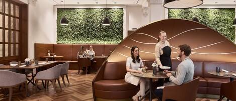 A modern restaurant with wooden flooring, leather seating, and a green wall with foliage.