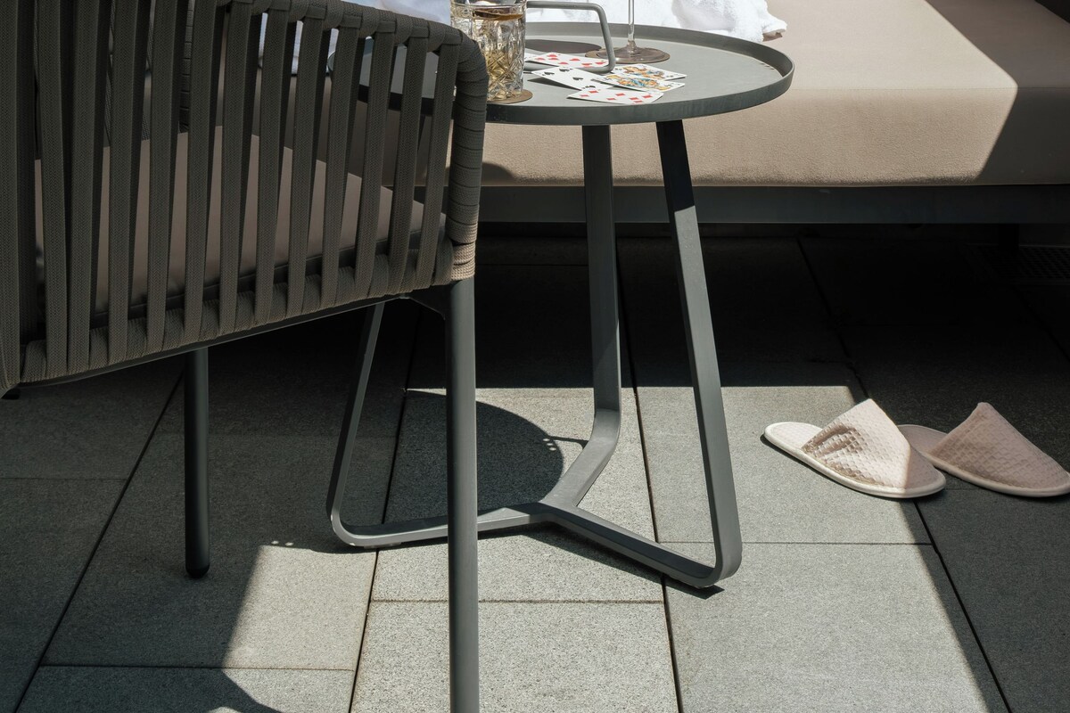 Un área de estar moderna al aire libre con una mesa redonda, un vaso de bebida y un par de pantuflas en el suelo.