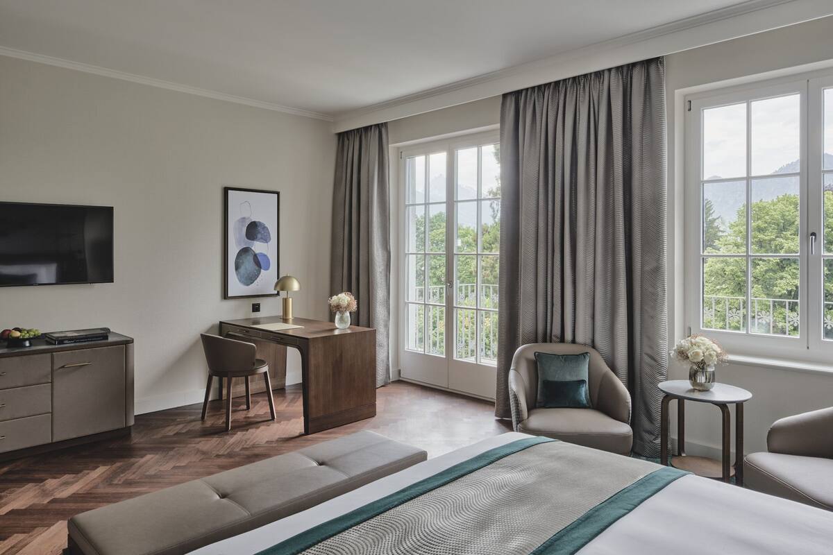 A hotel room with a bed, a desk, a chair, a sofa, and a TV.
