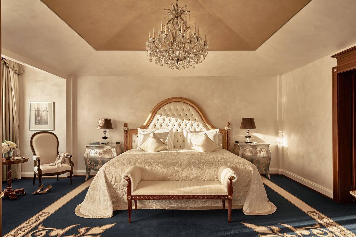 A spacious bedroom with a large bed, a chandelier, a chair, and a nightstand.