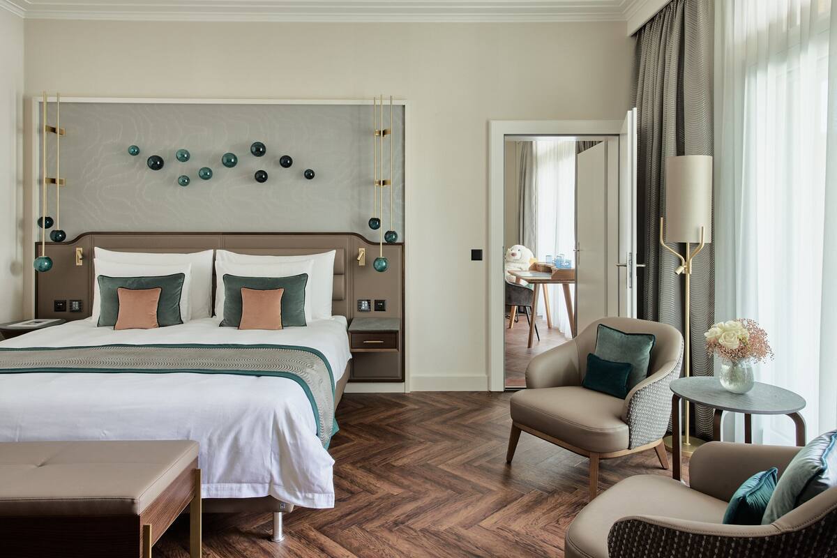 A hotel room with a large bed, a sitting area with a chair and a small table, and a decorative wall piece above the bed.