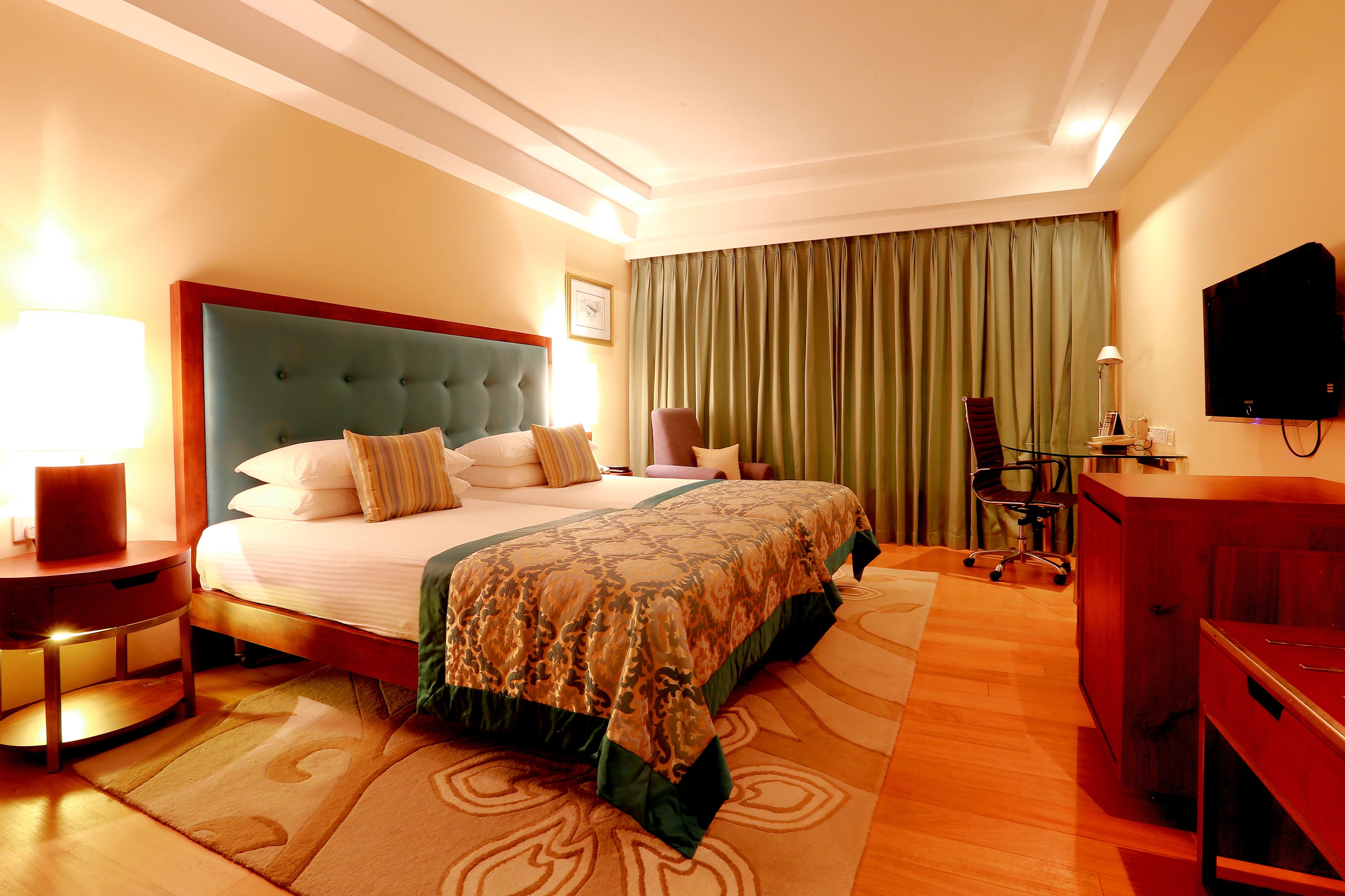Quarto de hotel com cama grande, escrivaninha, cadeira, televisão e abajur.