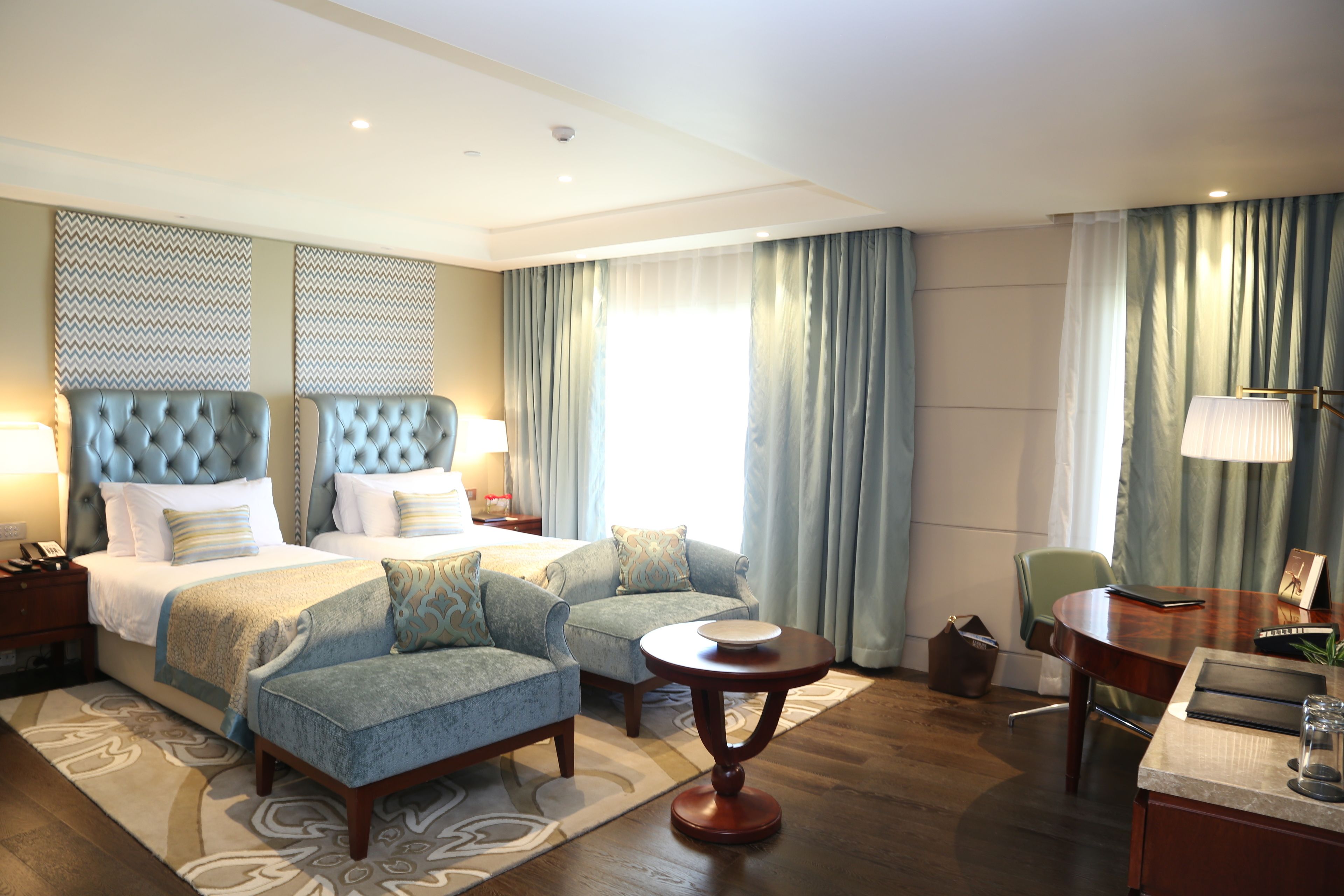 A hotel room with a large bed, two armchairs, a small table, a desk, and a chair.