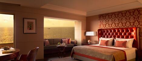 A hotel room with a large bed, a sofa, a desk, and a view of the sea.