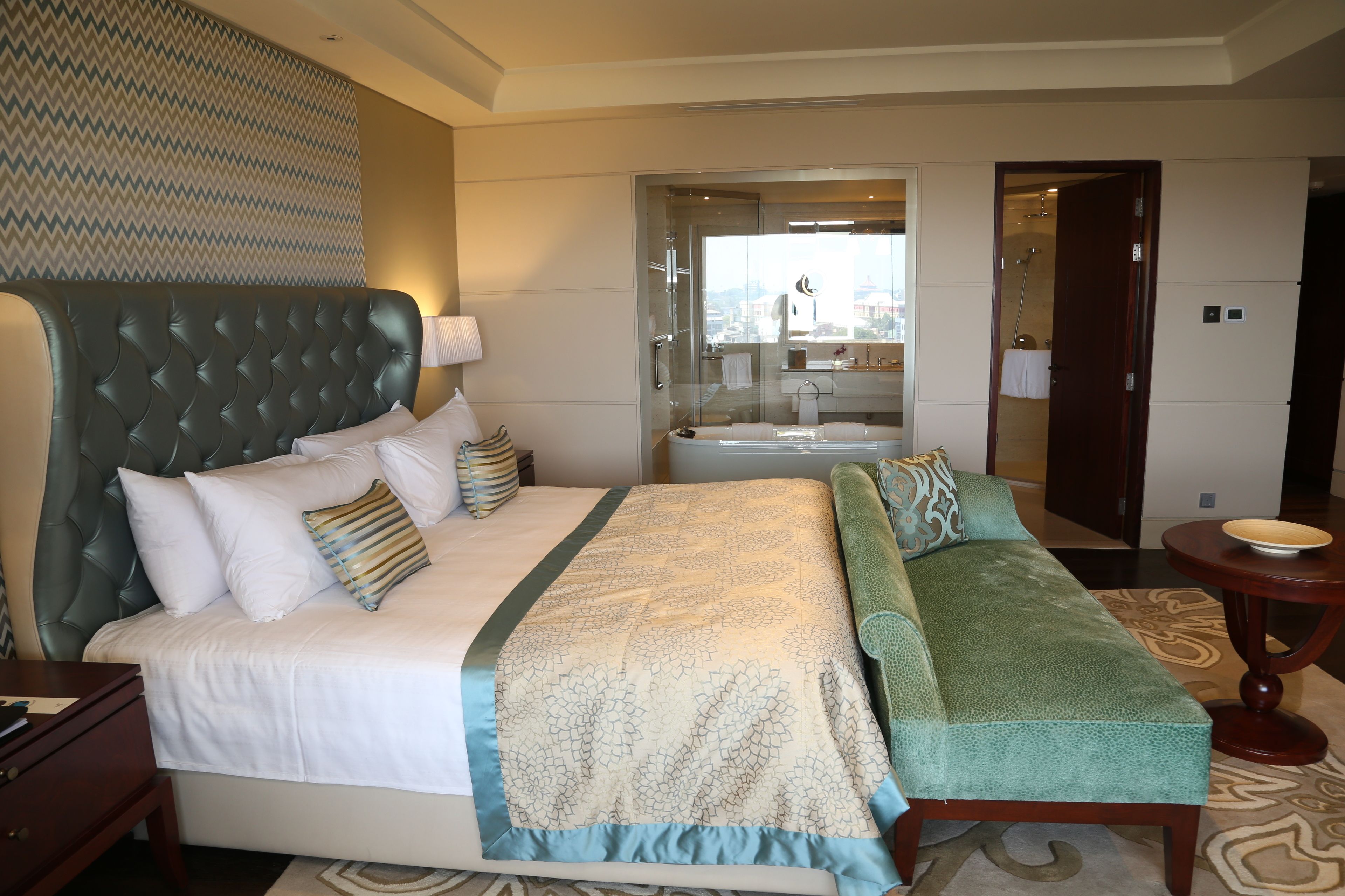 A hotel room with a large bed, a sofa, a bathroom with a bathtub, and a view of the city.