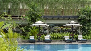 A pool area with lounge chairs and umbrellas, surrounded by lush greenery. - Taj Samudra (Colombo)