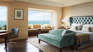 A hotel room with a view of the ocean, a sofa, a bed with a tufted headboard, a desk, and a chair. - Taj Samudra (Colombo)
