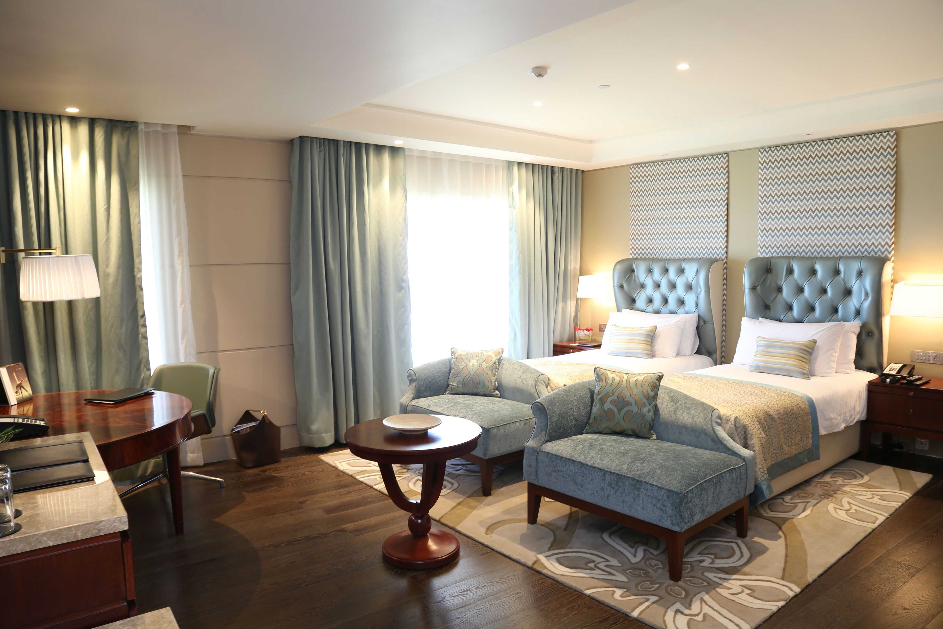 Een hotelkamer met een groot bed, twee fauteuils, een kleine tafel en een bureau met een lamp.