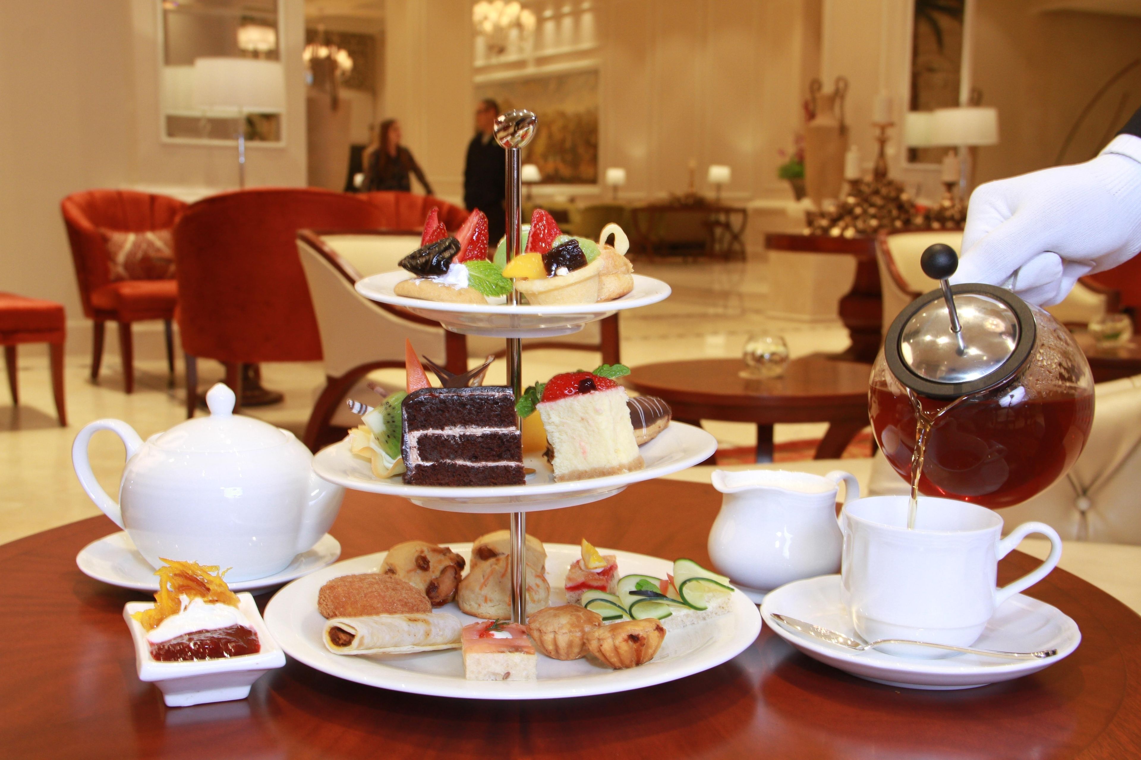 A three-tiered dessert stand with various pastries and a teapot pouring tea into a cup.