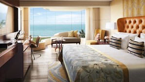 A hotel room with a large bed, a desk, a chair, a sofa, and a view of the ocean. - Taj Samudra (Colombo)