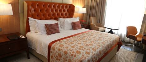 Une chambre d’hôtel avec un grand lit, deux tables de chevet, une chaise, une petite table et une fenêtre avec des rideaux.