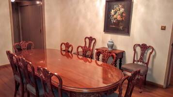 Un salón de conferencias con una mesa ovalada de madera rodeada de sillas ornamentadas, un jarrón sobre una mesita auxiliar y un cuadro de flores enmarcado en la pared.