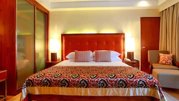 Una habitación de hotel con una cama grande, un armario de madera, un escritorio con lámpara y un área de descanso con una silla y un sofá.