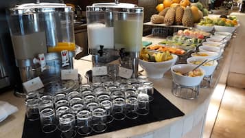 Una barra de bufet con varios dispensadores de bebidas, una variedad de frutas y varios cuencos de comida.