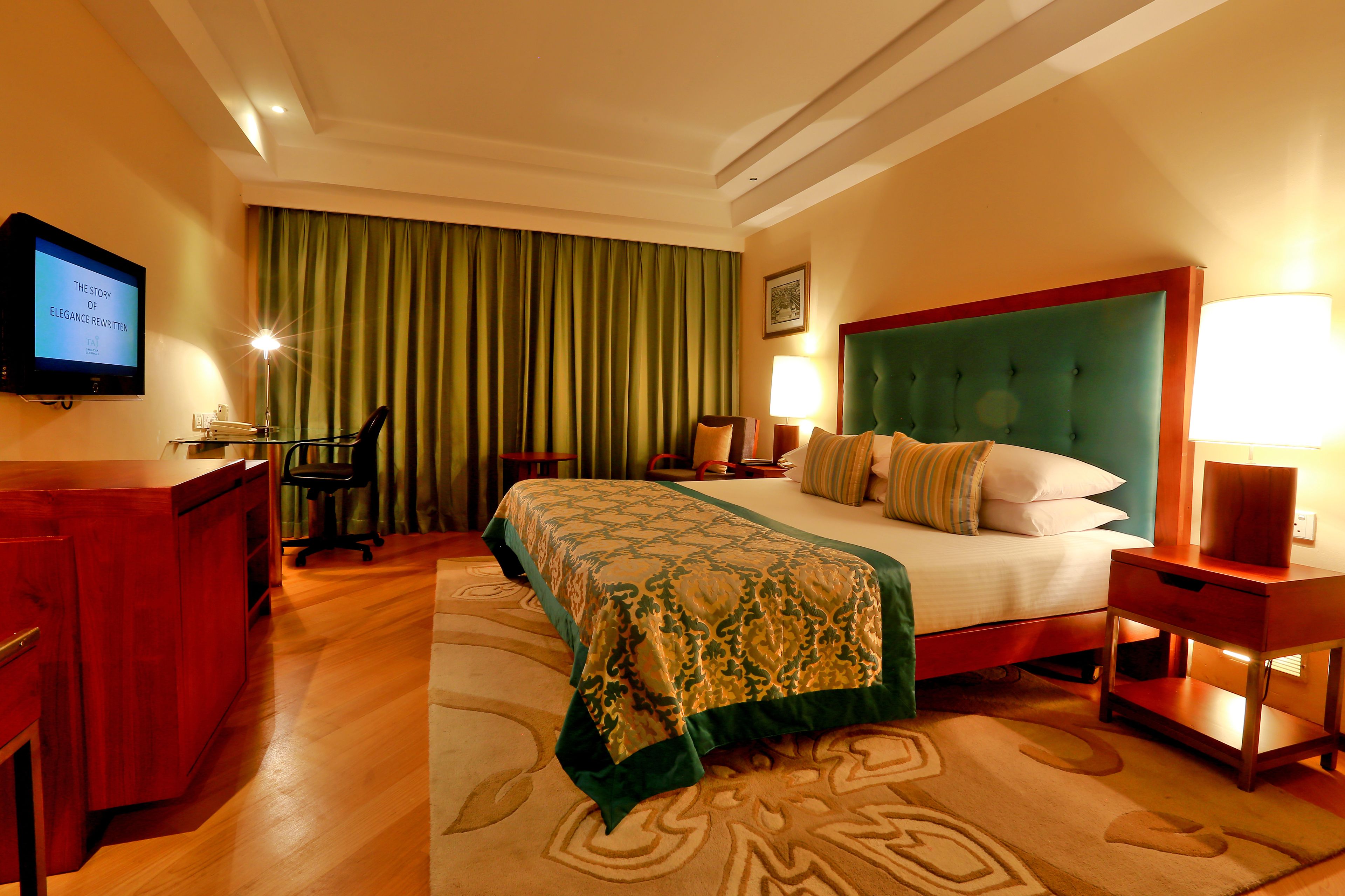 Una habitación de hotel con cama, escritorio, televisor y cortina verde.