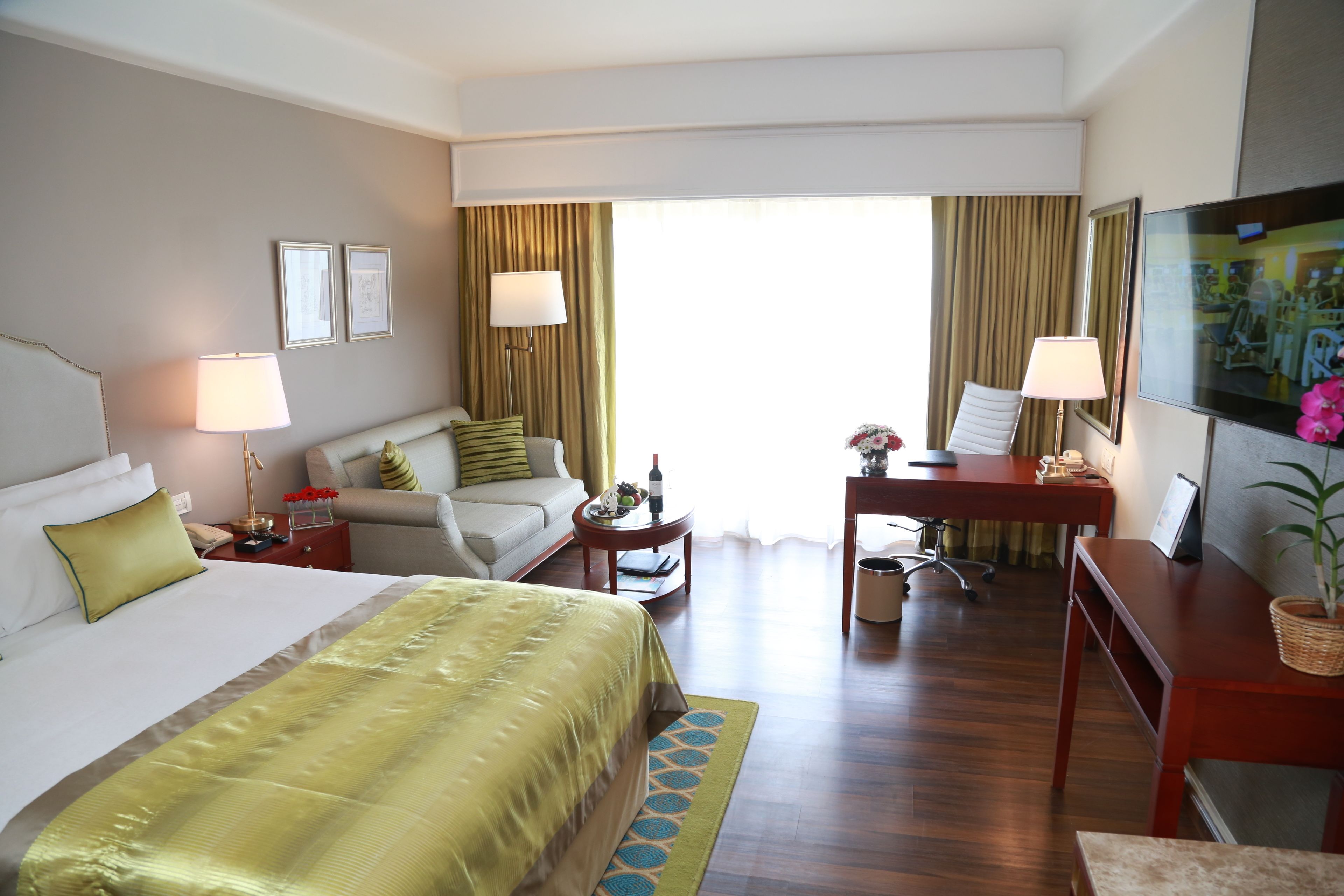 A hotel room with a large bed, a desk, a chair, a TV, and a window with curtains.