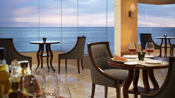 A dining area with a view of the sea, featuring round tables, chairs, and a table setting with wine glasses and a plate of food. - Taj Samudra (Colombo)