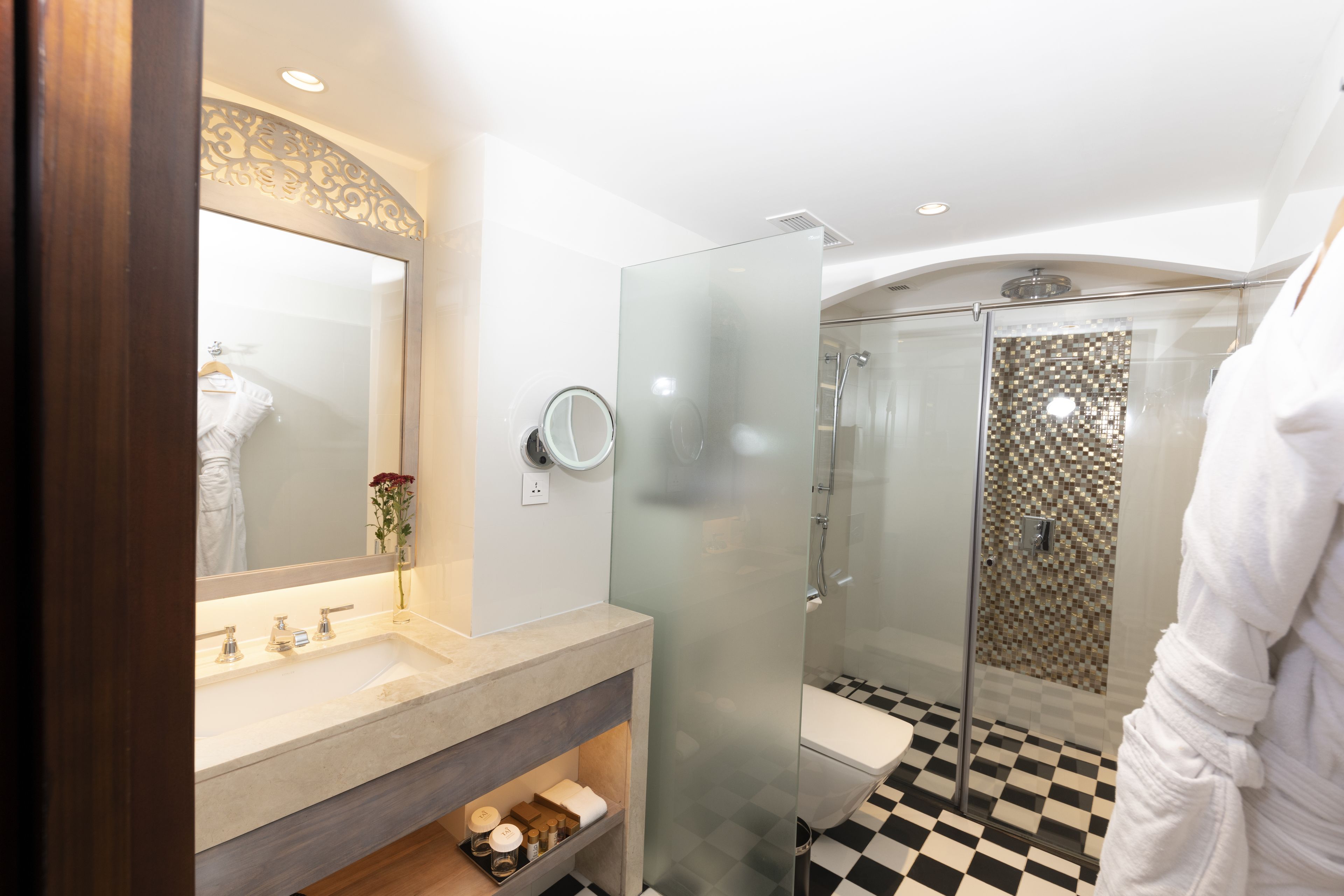 A modern bathroom with a glass shower enclosure, a large mirror, and a checkered floor.