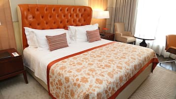 A hotel room with a large bed, a chair, a small table, and a lamp.