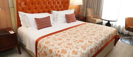 A hotel room with a large bed, a chair, a small table, and a lamp.