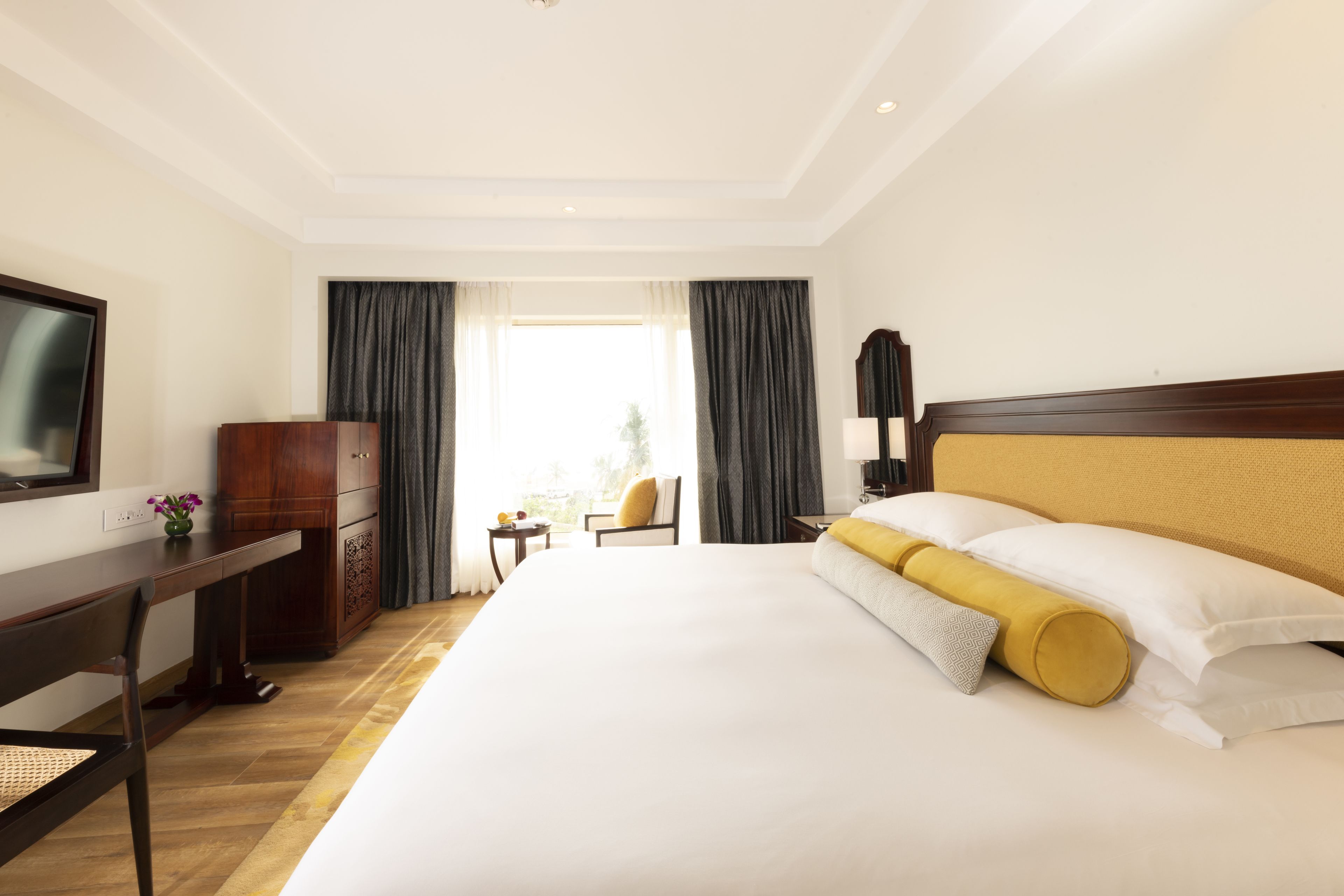A hotel room with a large bed, a wooden desk, a TV, and a view of the outdoors.