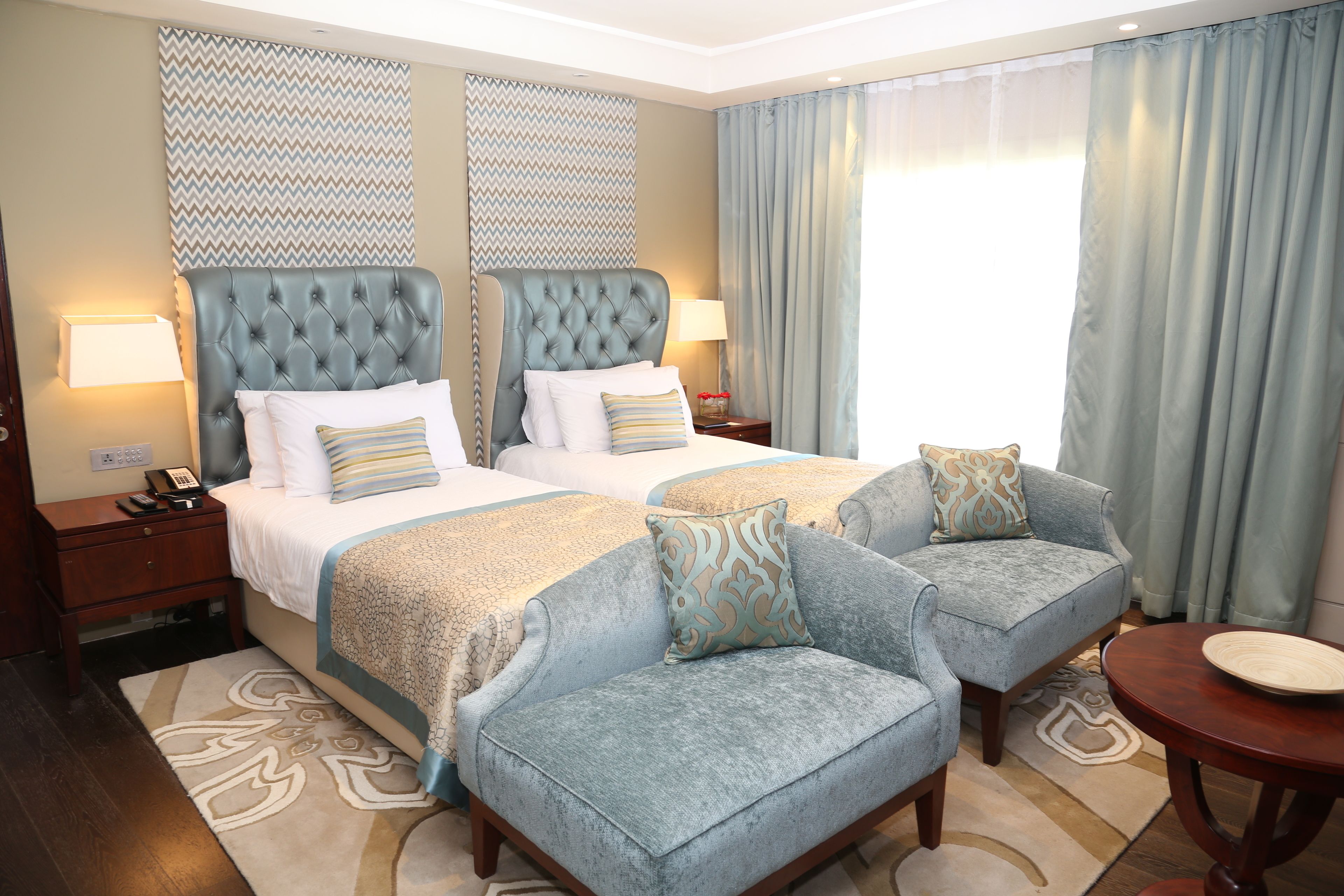 A hotel room with two beds, a sofa, a small table, and a patterned rug.