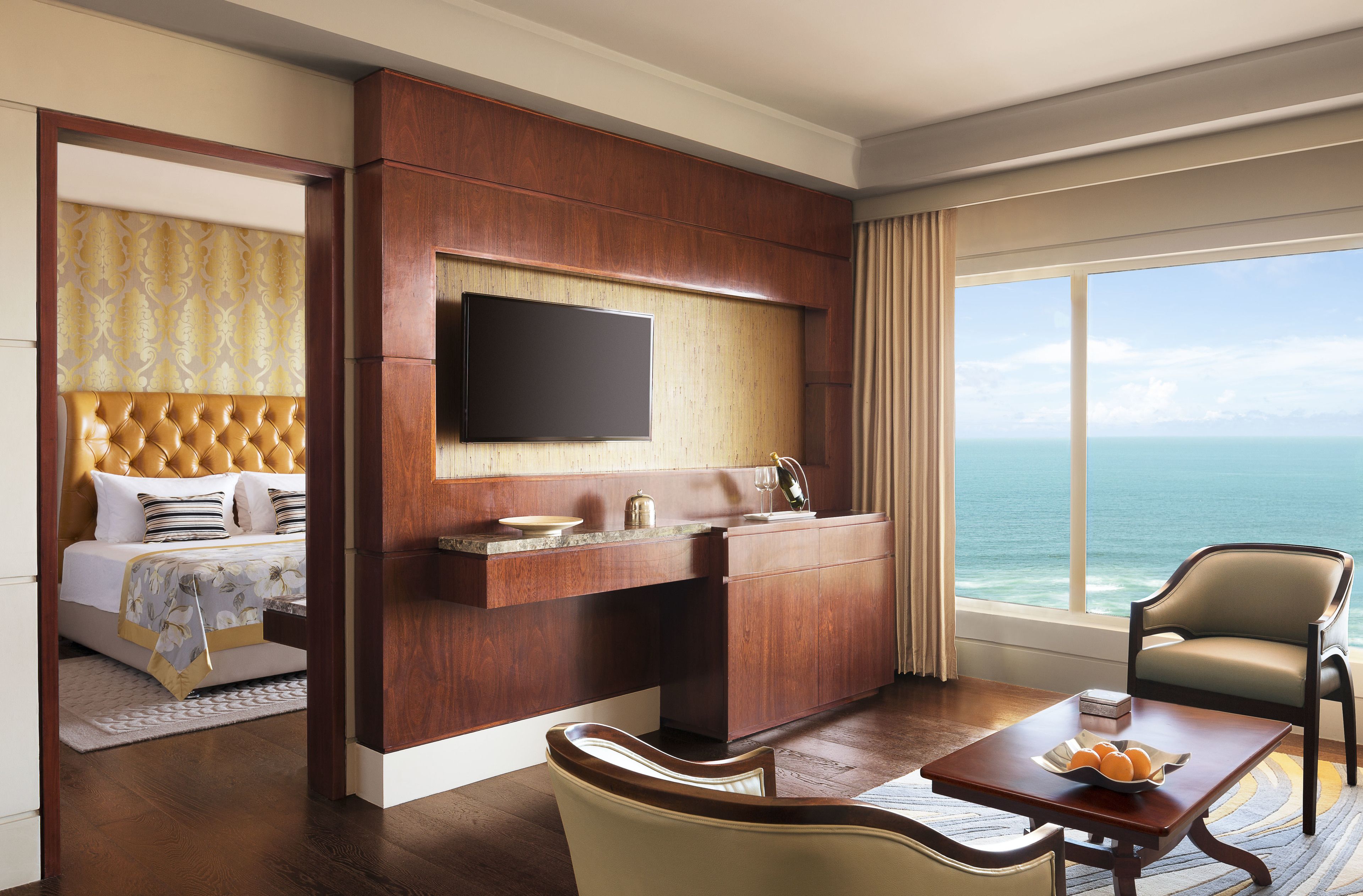 A hotel room with a bed, a TV, a desk with a chair, and a view of the ocean.