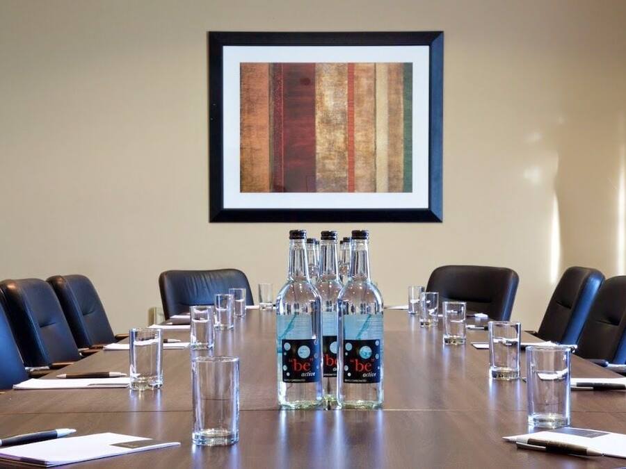 Une salle de conférence avec une longue table, des chaises en cuir noir et des bouteilles d’eau sur la table, portant l’inscription « soyez actifs ».