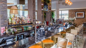 Una zona de bar con una barra alargada, varios taburetes y lámparas colgantes.
