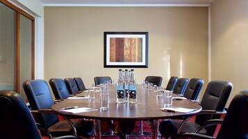 A conference room with a round table, black leather chairs, and a framed artwork on the wall.