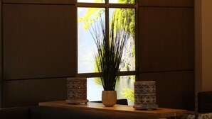 Una habitación con un ventanal grande, una planta en maceta y cojines estampados en un banco.