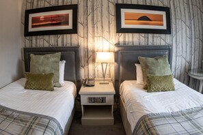A hotel room with two beds, a nightstand with a lamp, and two framed pictures on the wall.