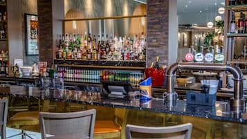 Een bar met verschillende drankflessen, een kassa en barstoelen.