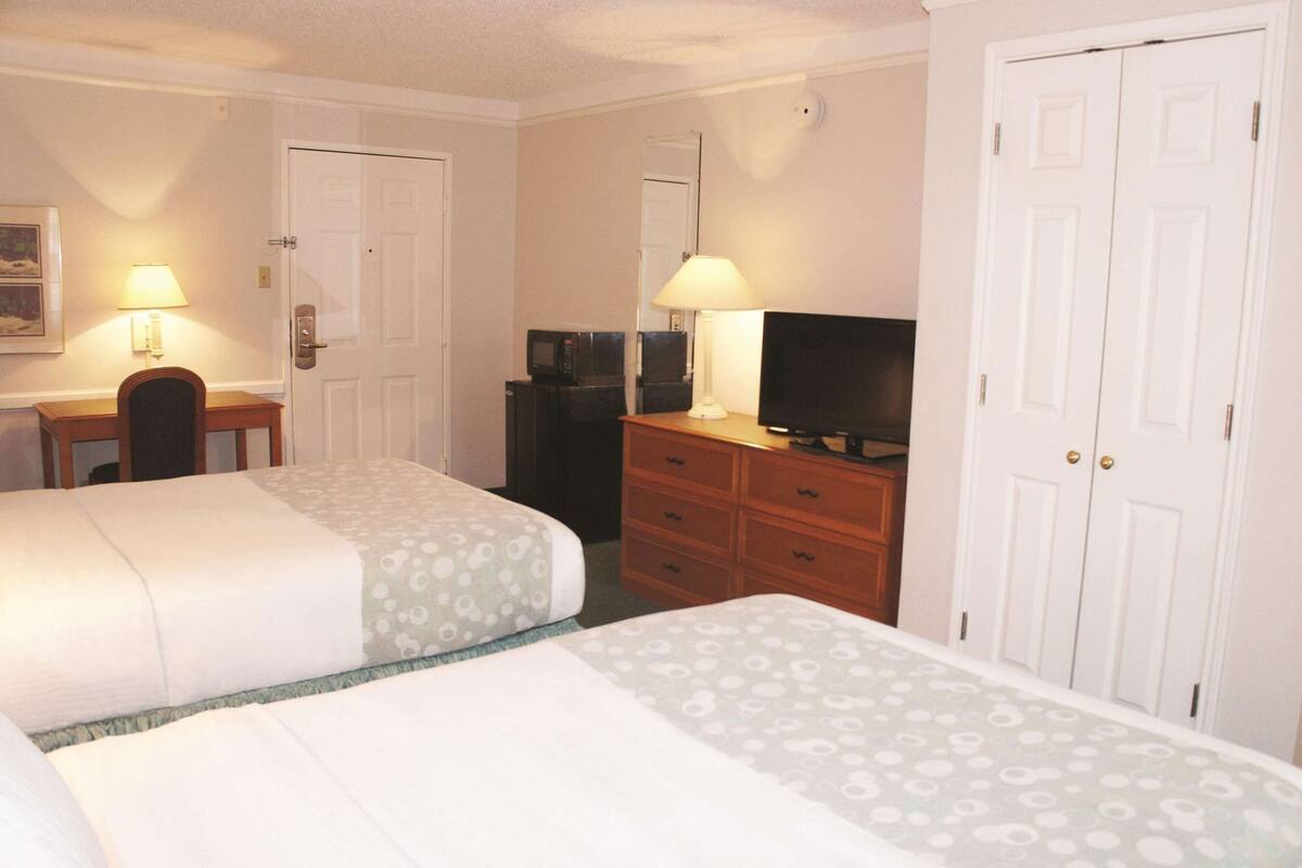A hotel room with two beds, a desk, a television, and a dresser.