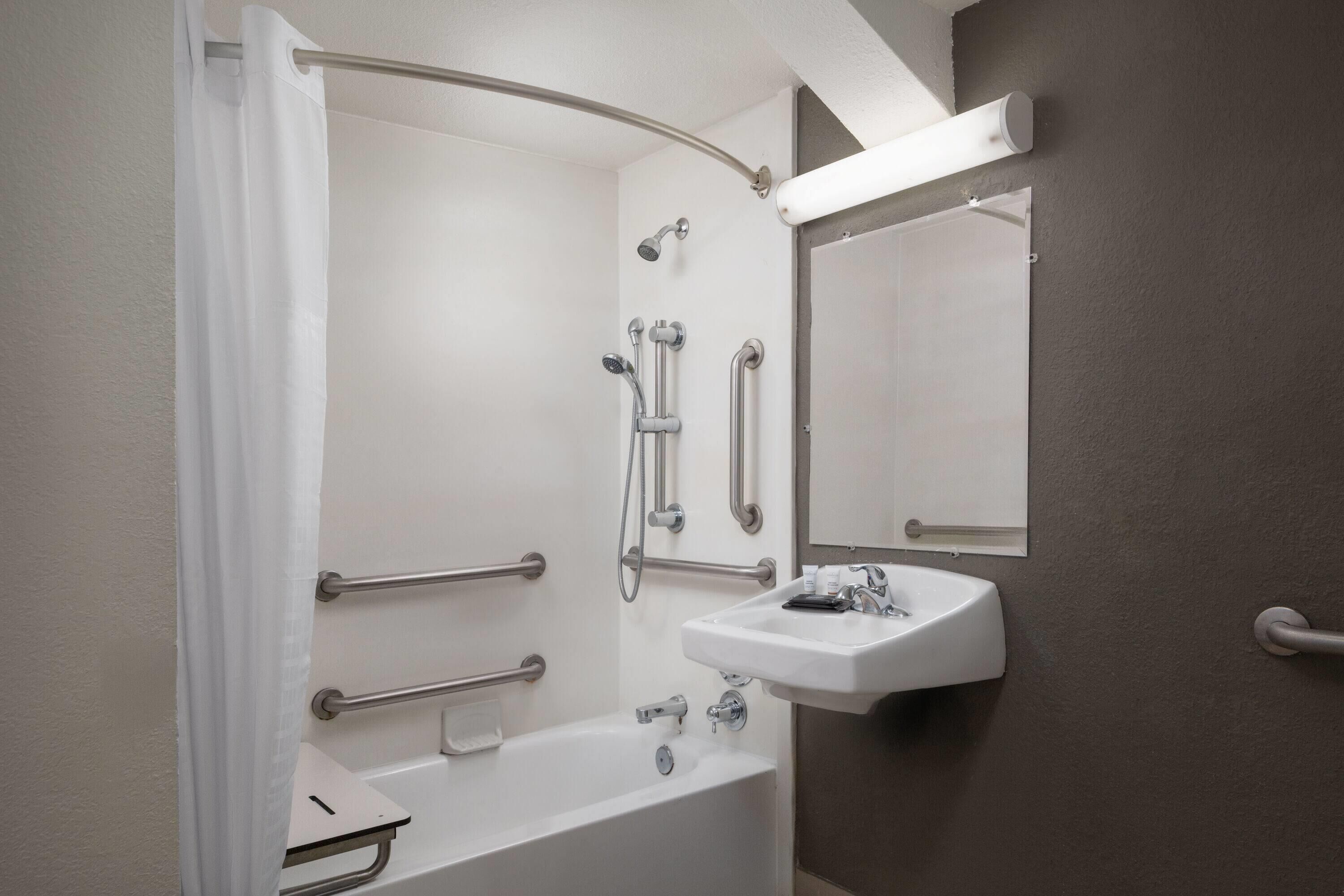 Un baño con bañera, lavamanos, ducha con barras de apoyo y un espejo.