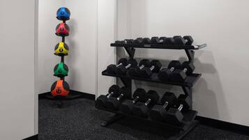A corner of a room with a wall-mounted dumbbell rack and a set of colorful medicine balls.