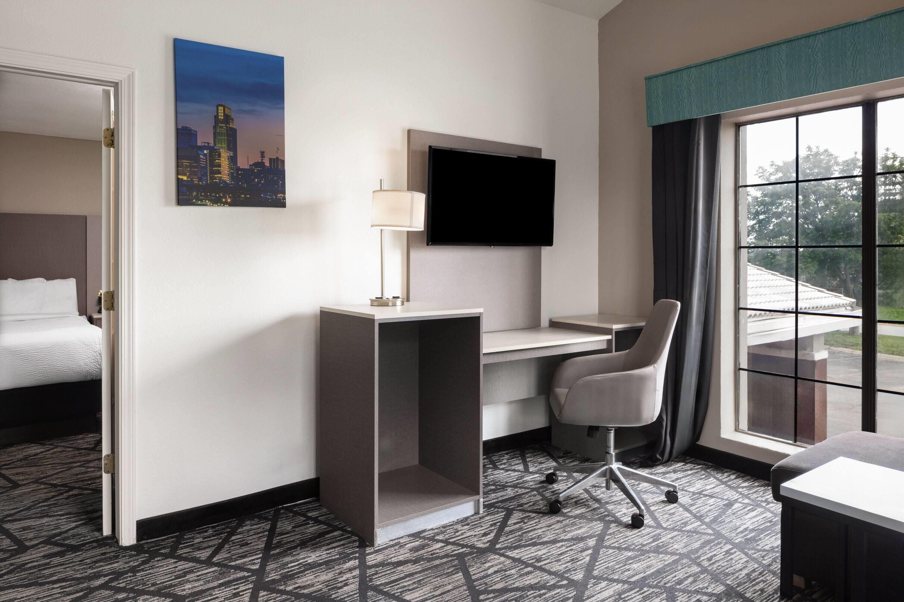 A hotel room with a bed, desk, chair, TV, and a window with a view.