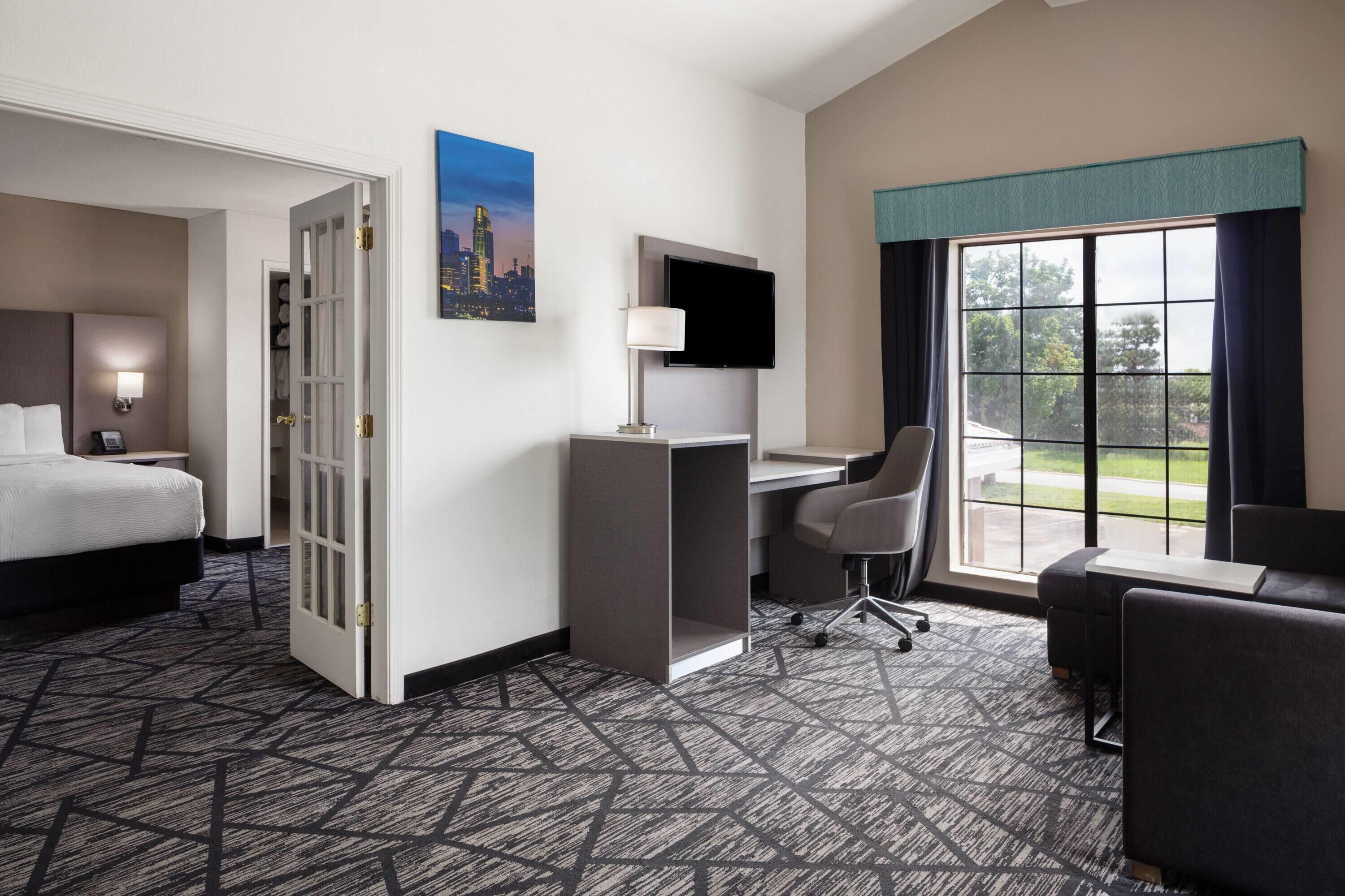 A hotel room with a bed, desk, chair, and a large window with a view.