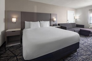 A hotel room with a large bed, bedside tables, a desk, a chair, and two wall-mounted lamps.
