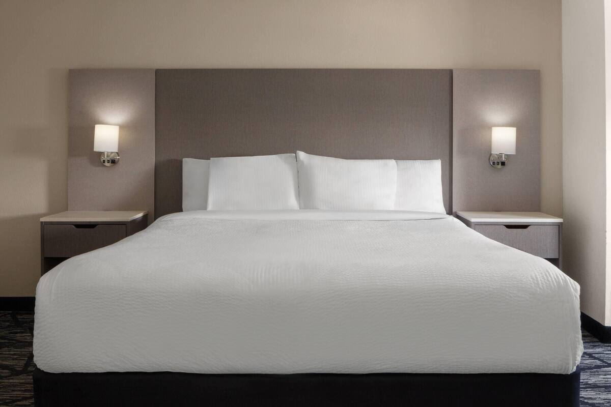 A hotel room with a large bed, two bedside tables, and wall-mounted lamps.