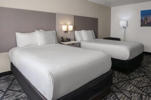 A hotel room with two beds, a nightstand, a lamp, and a cityscape painting on the wall. - La Quinta Inn by Wyndham Omaha West (Omaha)