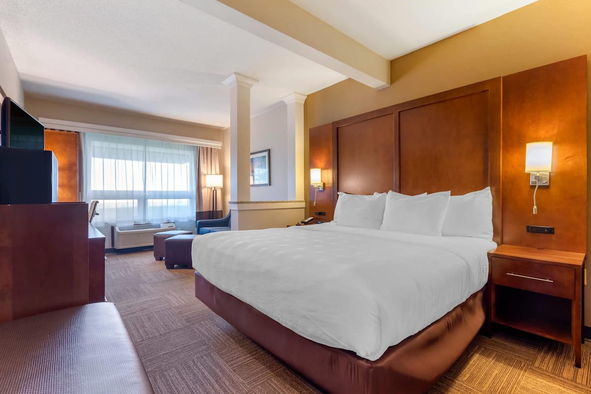 A hotel room with a large bed, a desk, a chair, and a window with curtains.