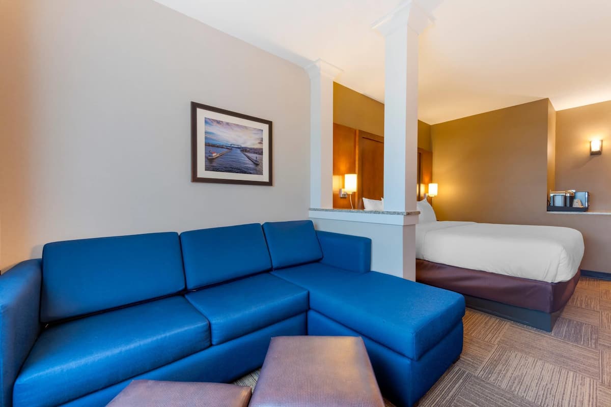 A hotel room with a blue sectional sofa, a single bed, a small table, and a framed picture on the wall.