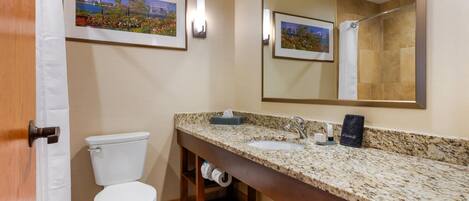 A bathroom with a toilet, sink, mirror, and framed pictures on the wall.