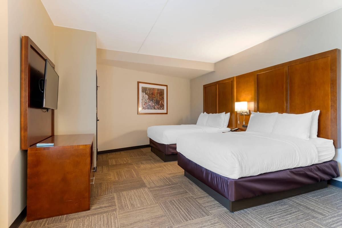 A hotel room with two beds, a wooden headboard, a flat-screen TV, a desk, and a framed picture on the wall.